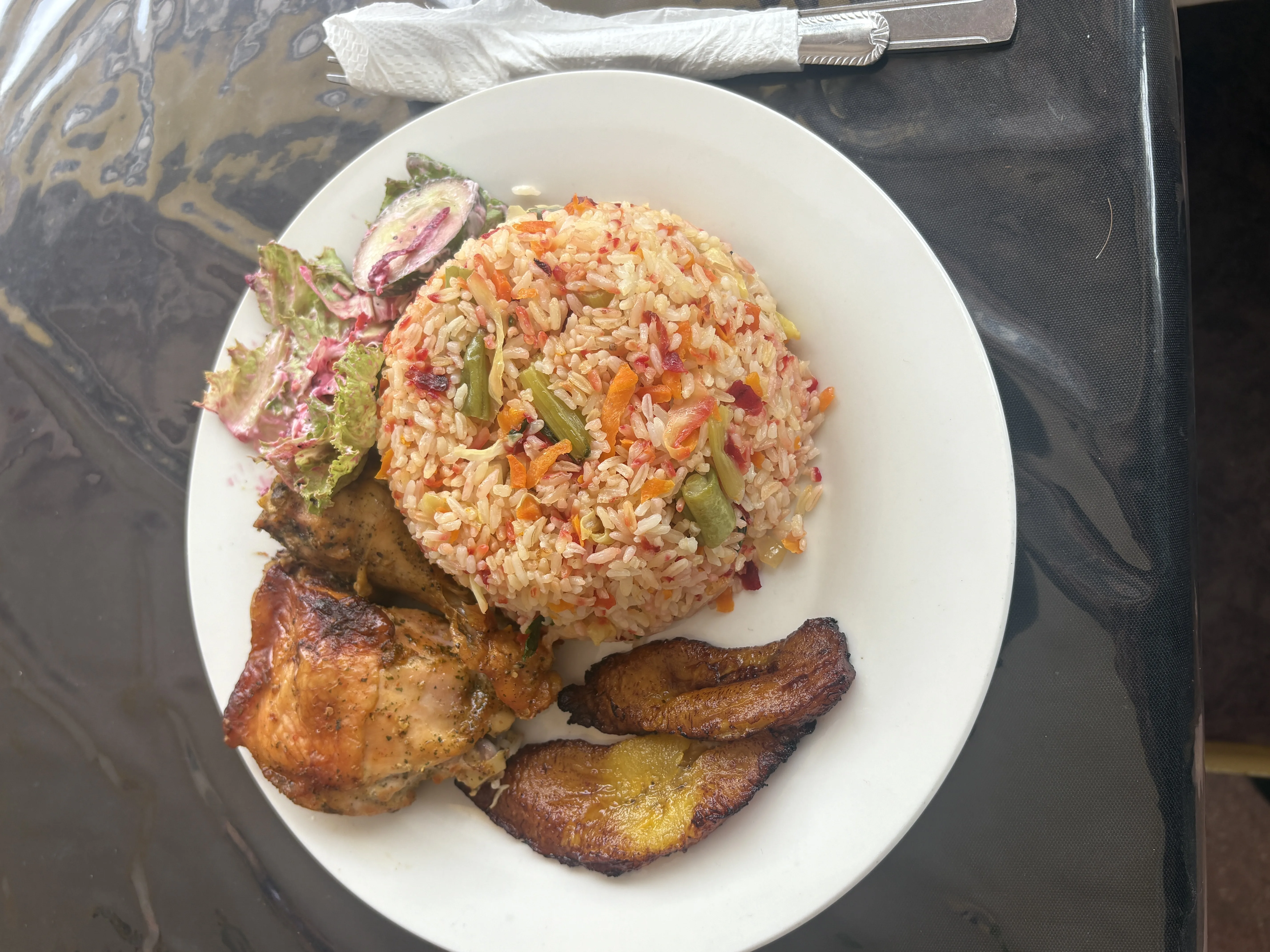 Pollo asado, arroz con vegetales, plátano y ensalada en plato blanco.