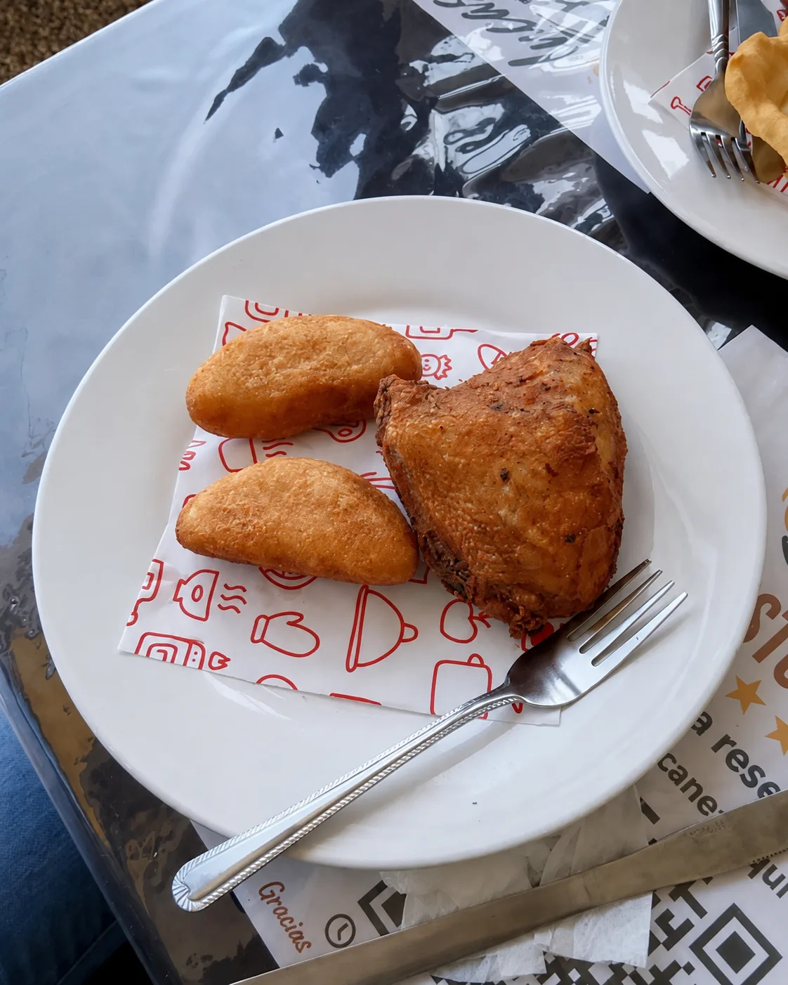 Pollo frito con dos piezas de masa frita en un plato blanco.
